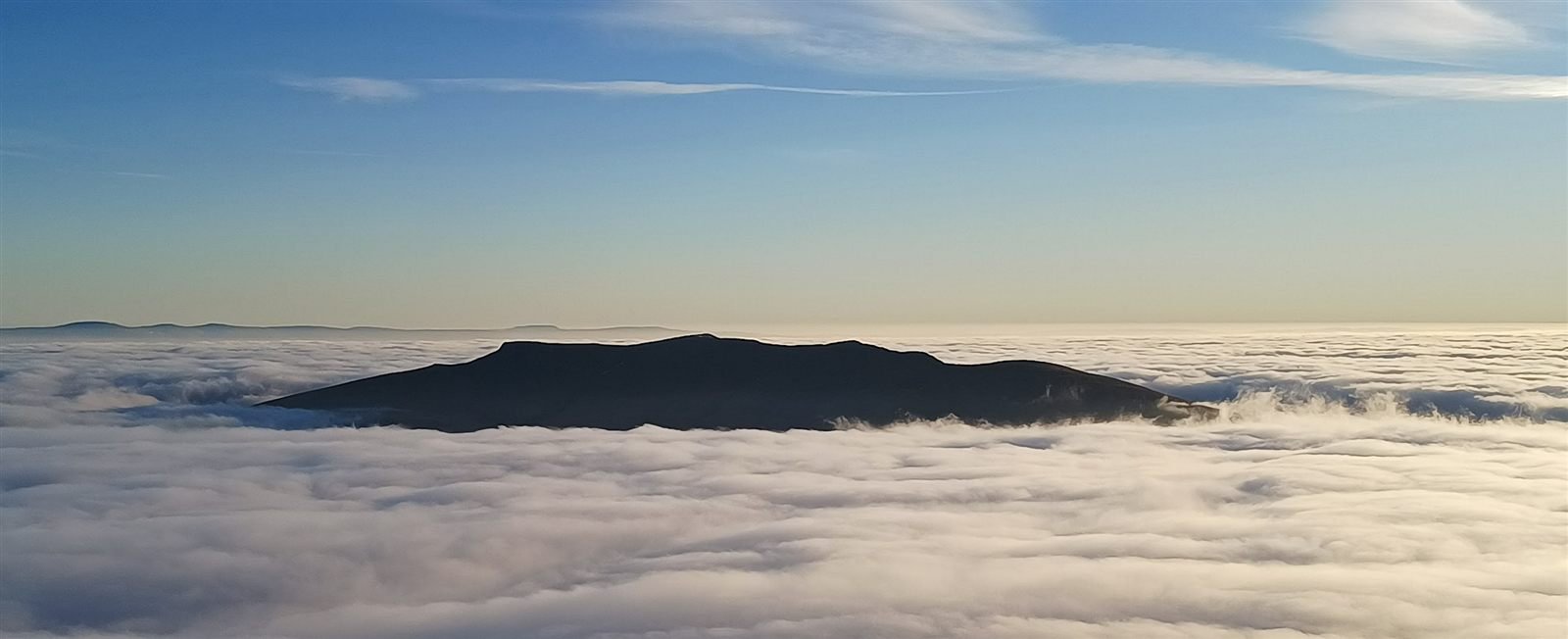A fell summit rising like an island from an unbroken sea of cloud beneath a blue sky