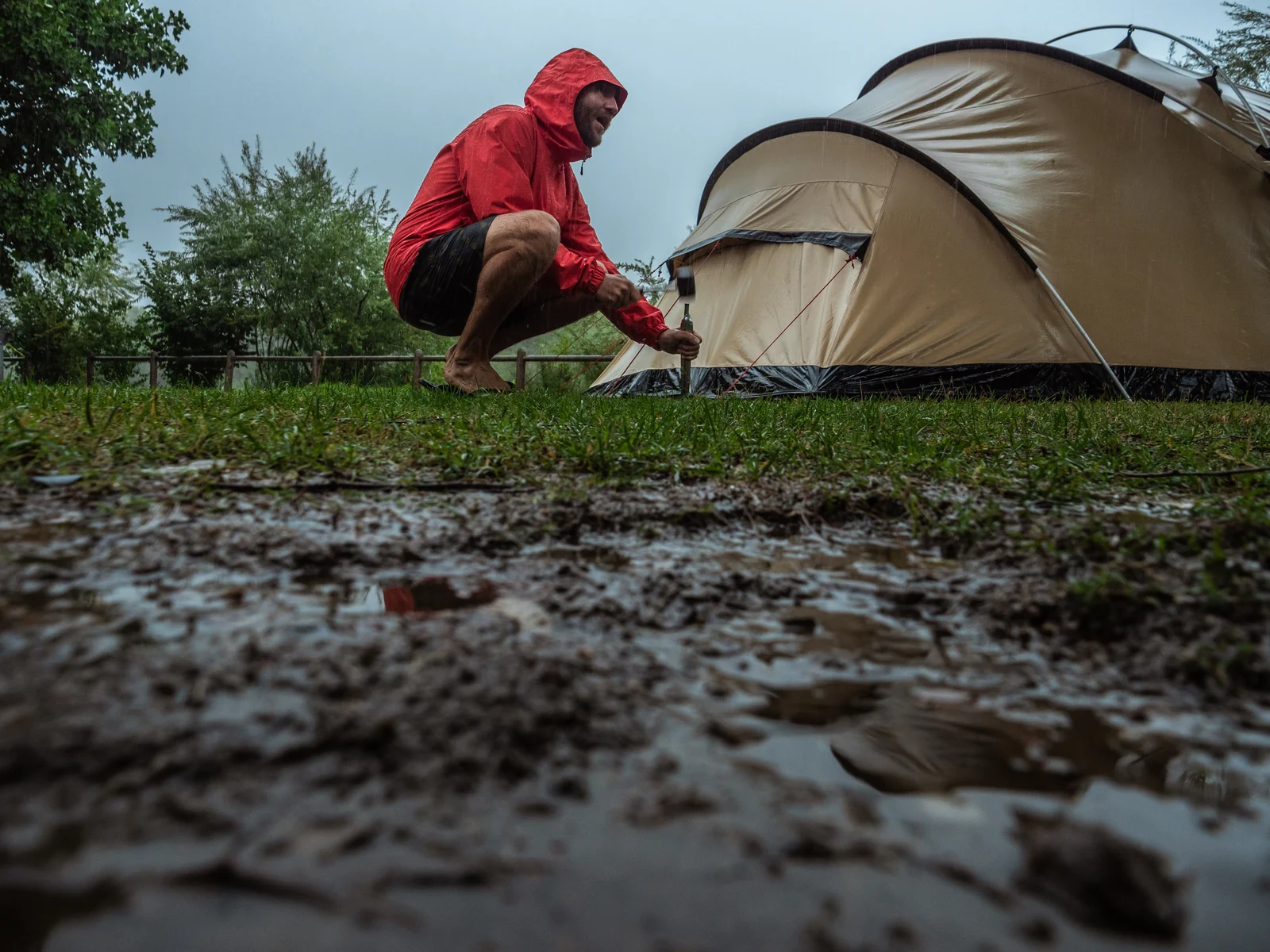 A camper beside a tent, with rainwater and muddy ground in the foreground