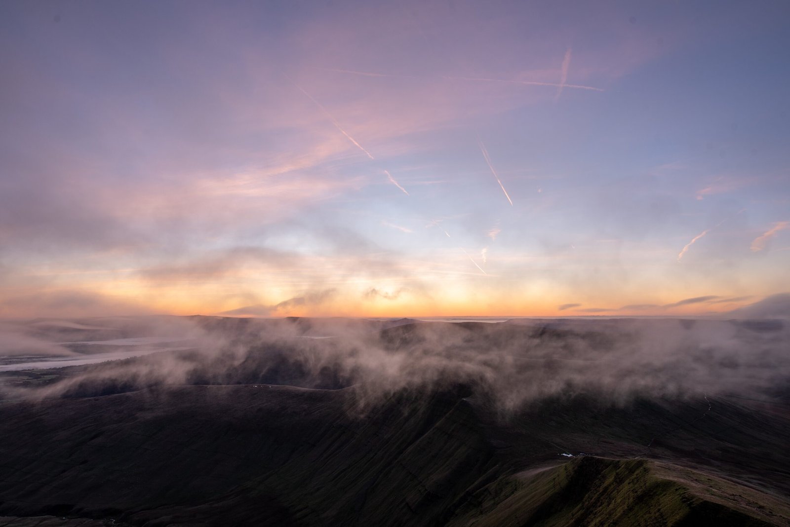Pink dawn sky above mist drifting across mountain ridges in Bannau Brycheiniog